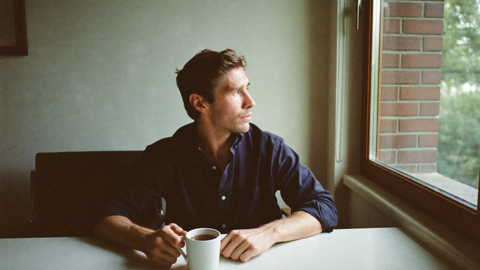 Unternehmer sitzt nachdenklich mit einer Tasse Kaffee am Fenster